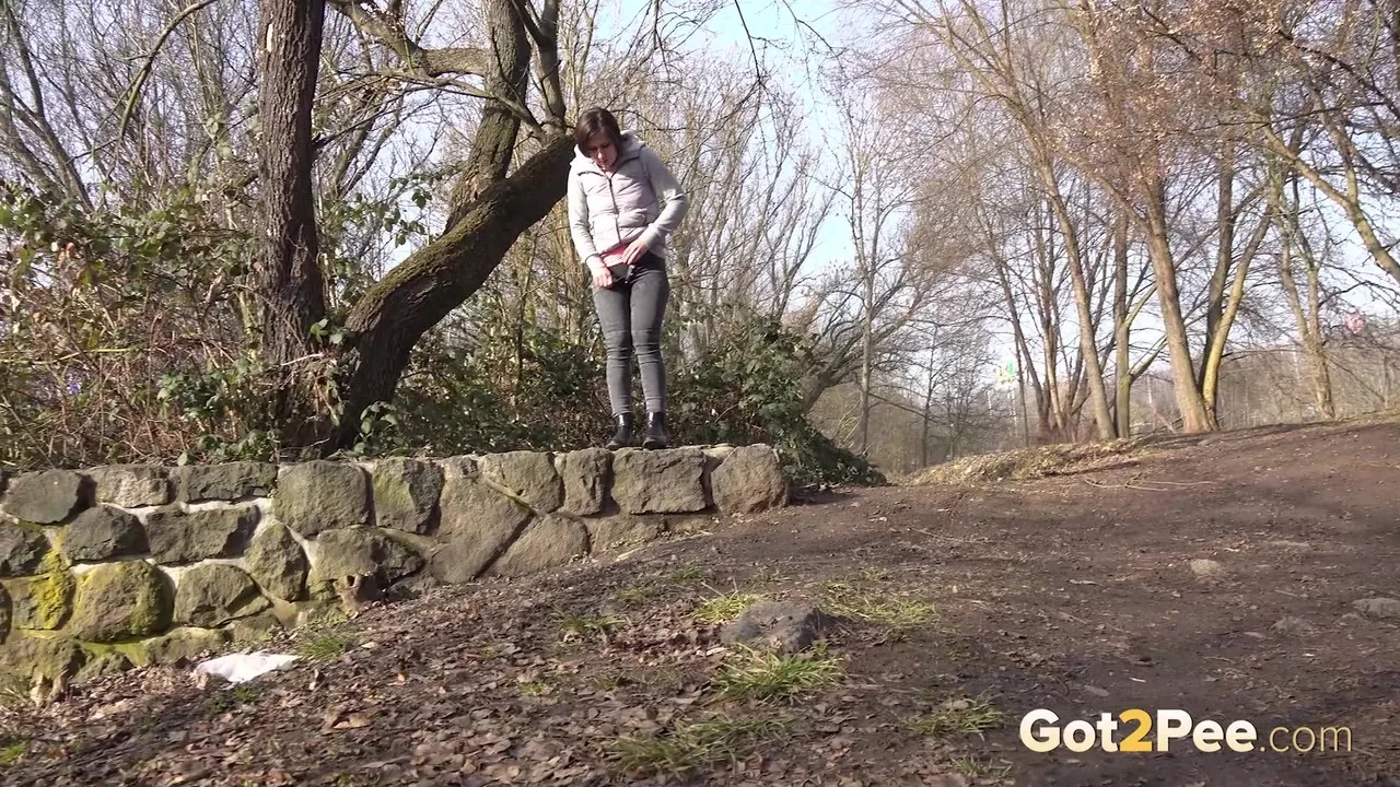 Inside Caucasian girl Lara Fox pee atop a stone retaining wall in the country — Featured